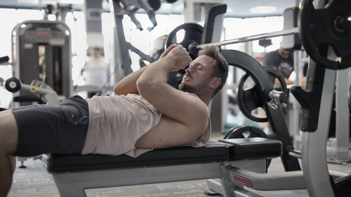Focused muscular sportsman in modern sportswear preparing to workout with heavy barbell on bench training in modern gym